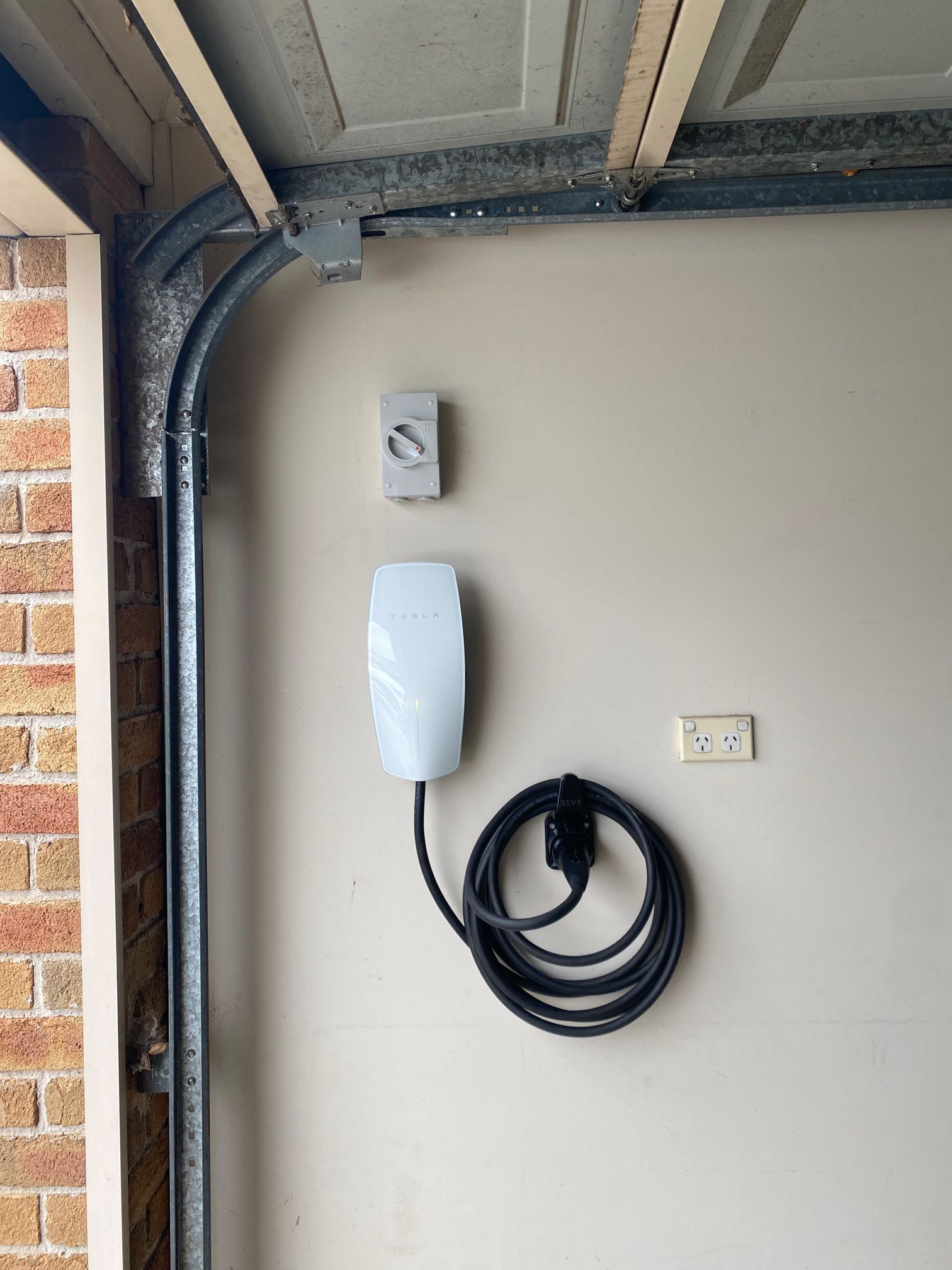 Tesla Gen 3 Wall Connector in a Castle Hill garage with an isolating switch above and an EV cable holder mounted below and to the right, cable coiled around it